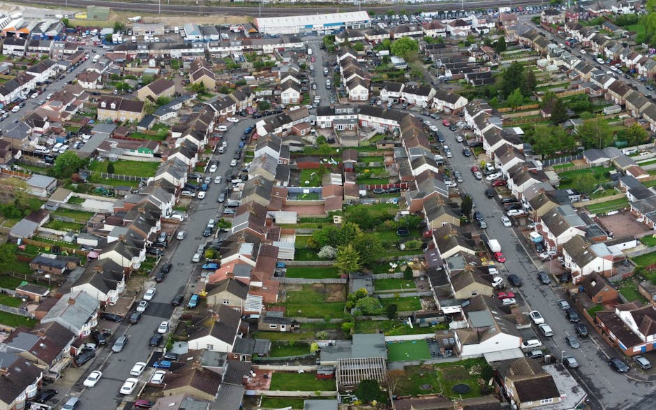 An aerial view of a densely packed residential neighborhood in Walthamstow Village, featuring closely situated terraced houses with varying roof styles, narrow streets lined with parked cars, and smal