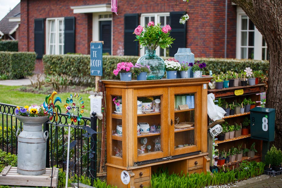 A charming front garden in Walthamstow Village featuring a small wooden display cabinet with glass doors, filled with decorative ceramics and household items. On top of the cabinet, there are various 